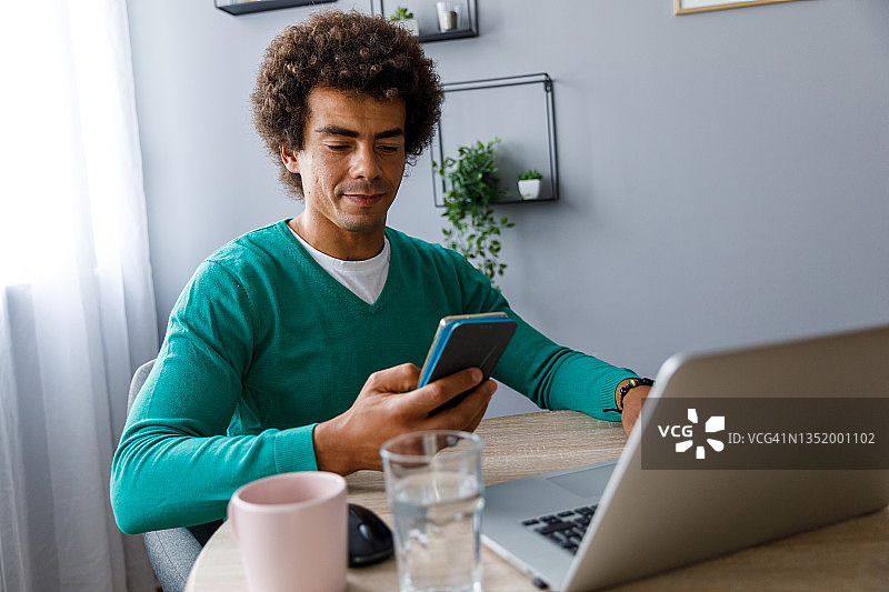 年轻男人坐在桌旁用智能手机发短信图片素材