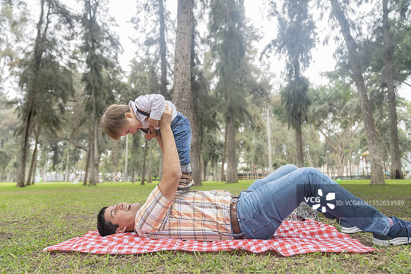 男人躺在公园里，用手臂举起儿子图片素材