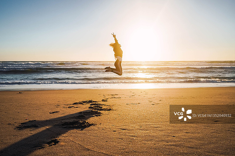 女人在日落时分的海滩上跳跃图片素材