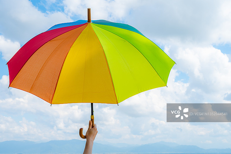 有人手持彩虹伞，背景是明亮的天空图片素材