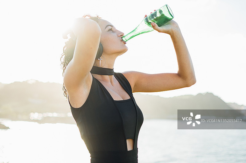 喝瓶装绿色啤酒并听音乐的年轻女人图片素材