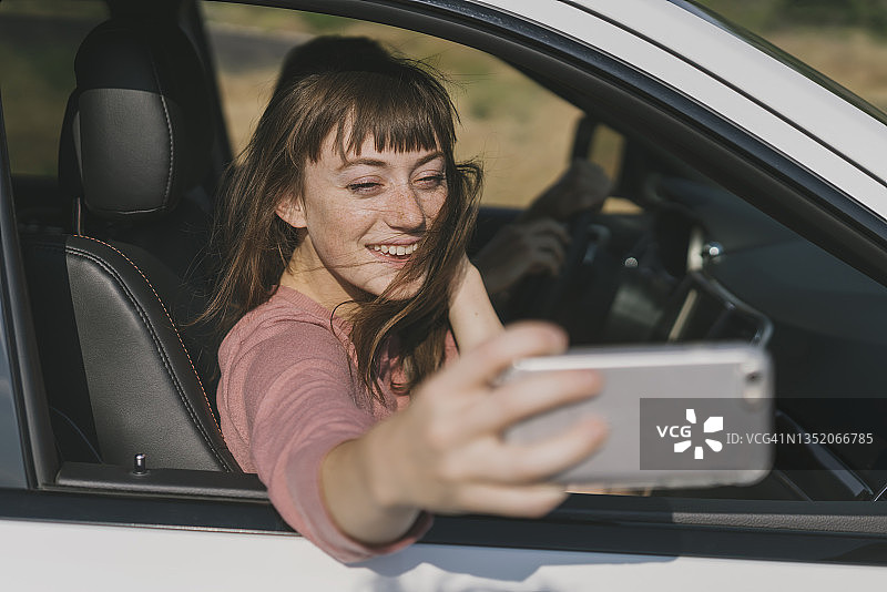 周末公路旅行中，在车里用智能手机自拍的快乐女人图片素材