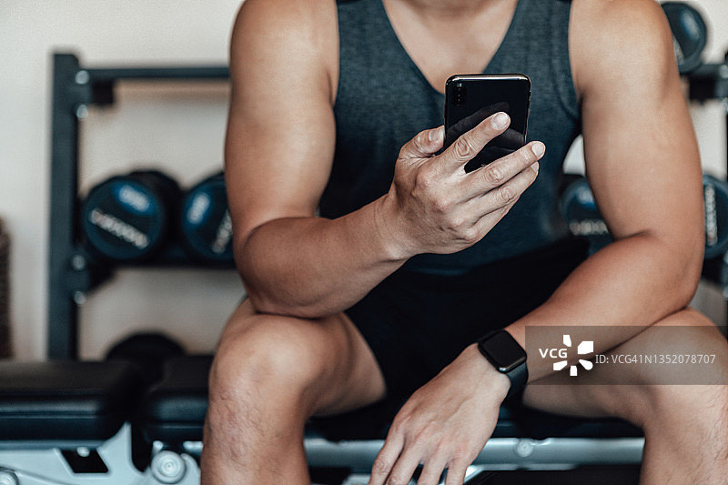 坐在健身房使用智能手机的健壮男人图片素材