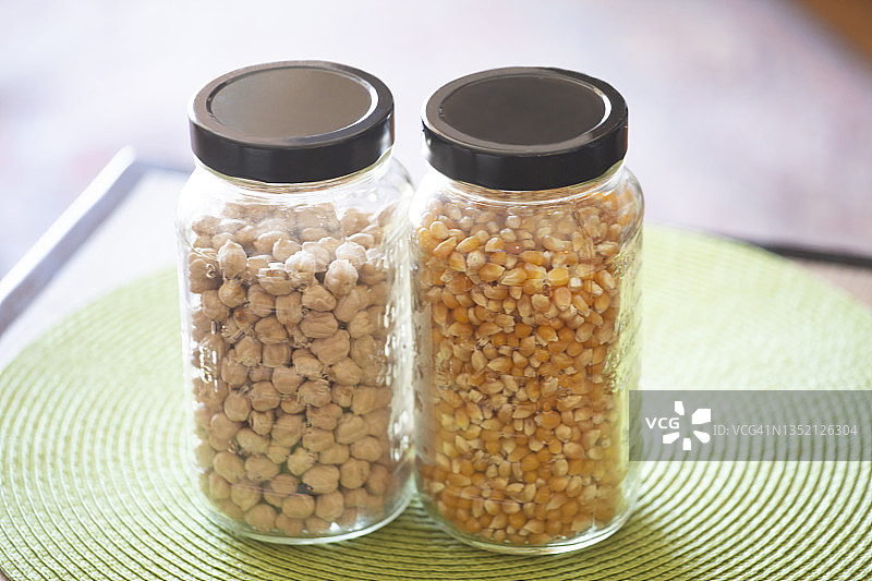 桌子上绿色餐垫上的两罐鹰嘴豆和玉米粒图片素材