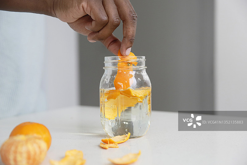非裔美国男人在明亮厨房将橘子皮放入玻璃罐的手部特写图片素材