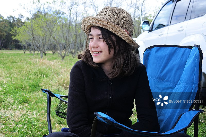 快乐的年轻女孩坐在房车旁的蓝色户外椅上图片素材