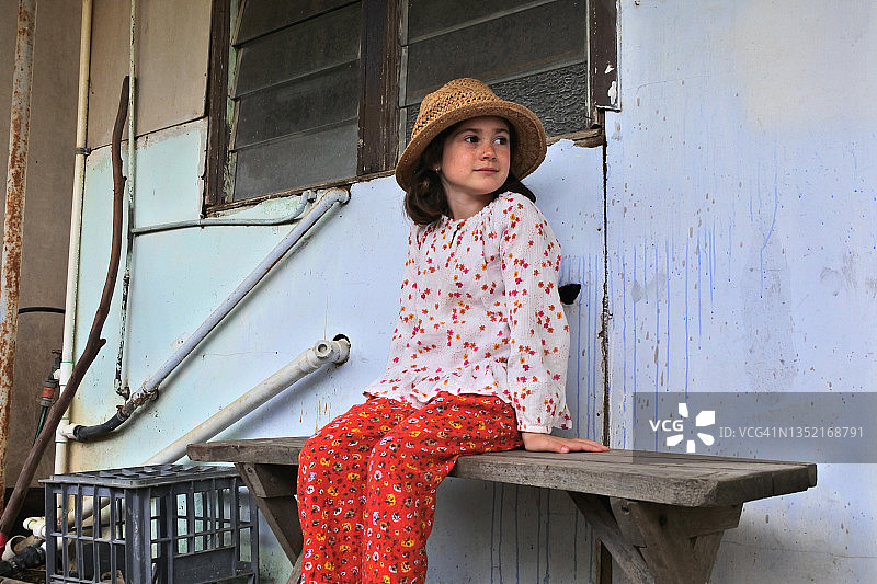 可爱少女坐在古老废弃农舍旁的木凳上图片素材