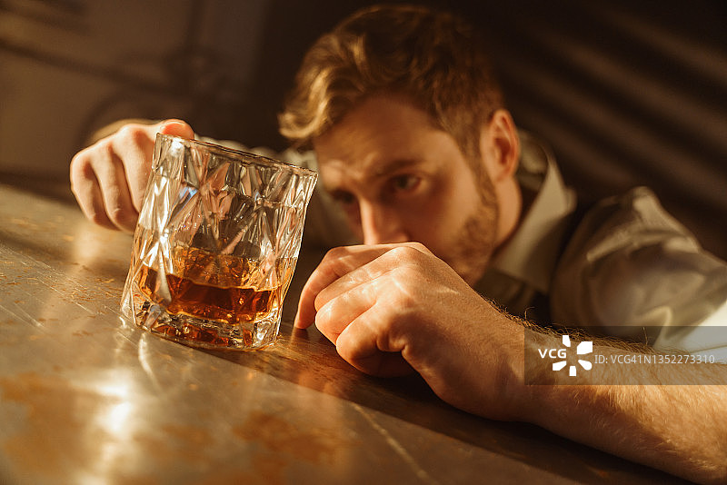 醉酒男子在桌旁手持威士忌的特写图片素材