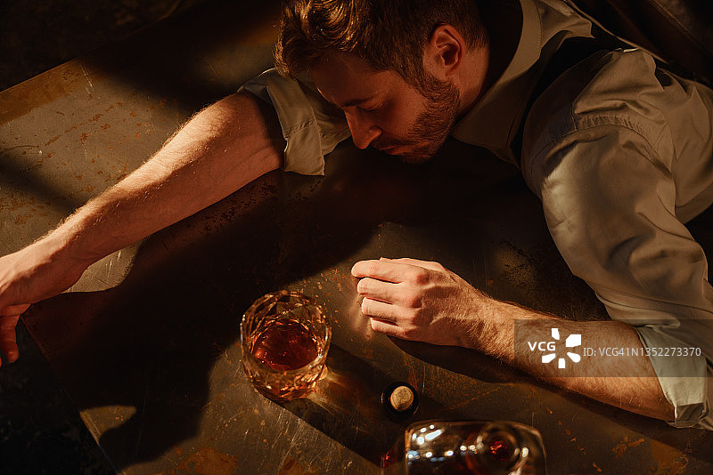 醉酒男子在桌旁手持威士忌酒杯的氛围肖像图片素材