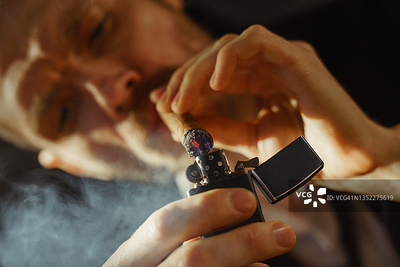 英俊男子在黑色背景下点燃雪茄的特写图片素材