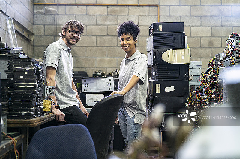 站在堆满电子垃圾的储藏室里的男女回收工人图片素材