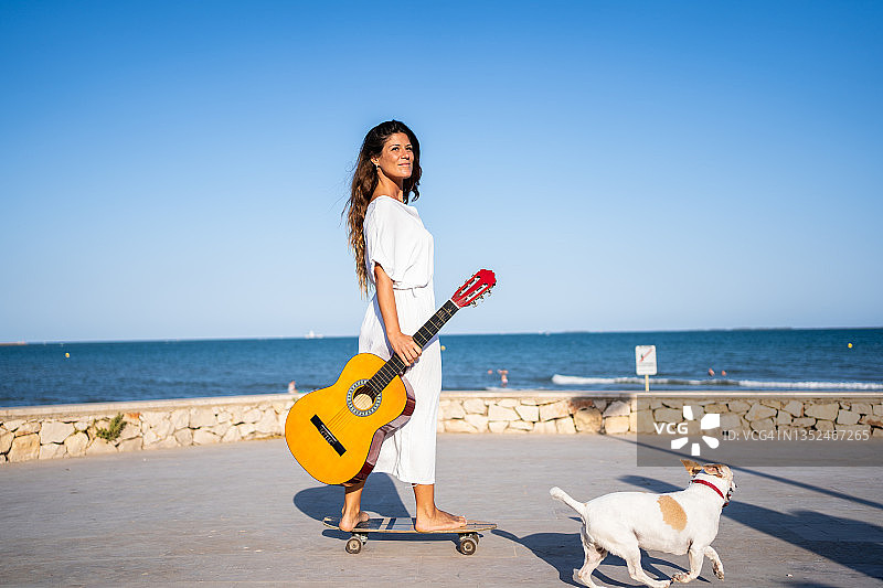 女人滑冰，手持古典吉他，小狗在海边跟随图片素材