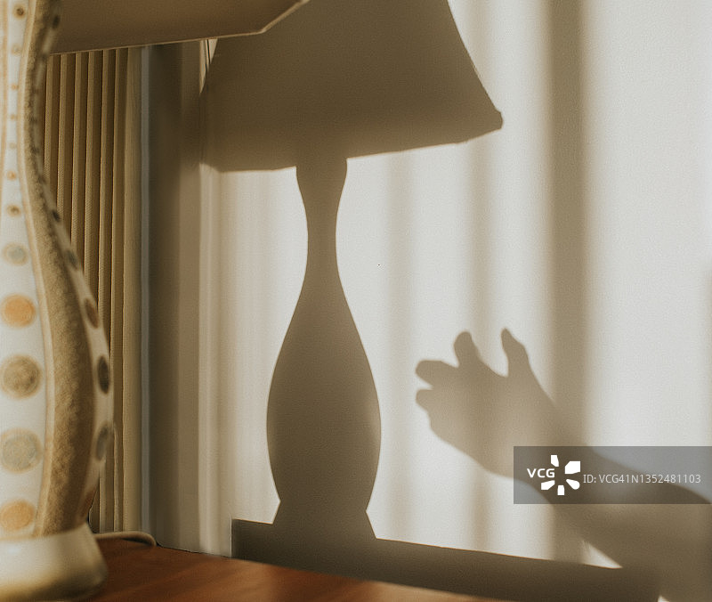 手伸向旧台灯并打开，灯光在墙上投下阴影图片素材