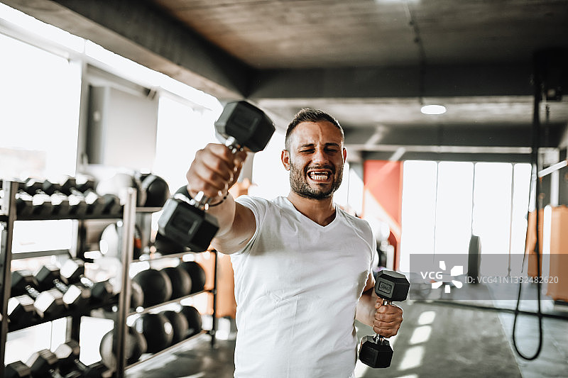 男人在健身房用哑铃锻炼肩部力量图片素材