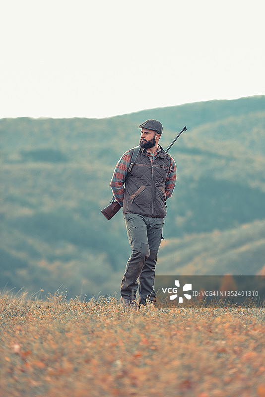 留着黑色胡须，拿着枪走在土路上的健壮年轻猎人图片素材
