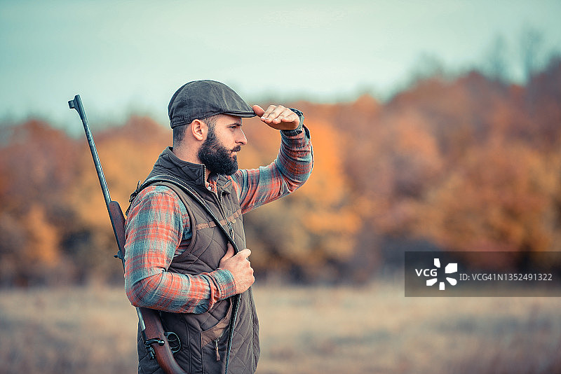 留着黑色胡须，拿着枪走在土路上的健壮年轻猎人图片素材