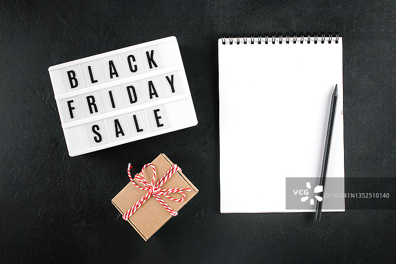 灯箱上显示的黑色星期五促销字样、礼品盒、黑色背景上带有文本位置的空白笔记本。平铺，顶视图图片素材