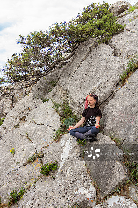 专注的女孩在岩石上以莲花坐姿练习瑜伽图片素材