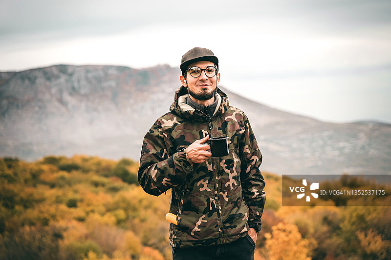 年轻帅气的旅行者面带微笑，休息时享受一杯热咖啡图片素材