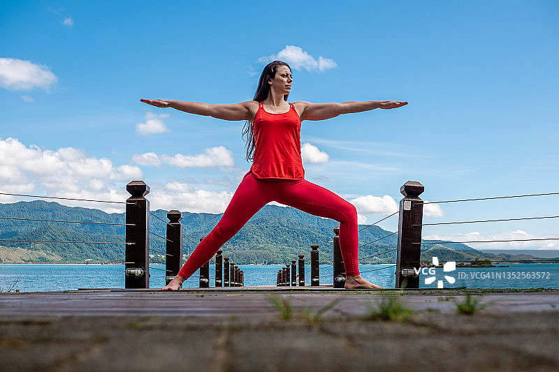美丽的女人在岛屿海岸附近的木制码头上练习瑜伽。黎明时的电影背景图片素材