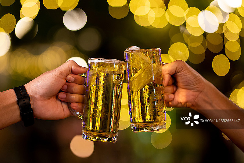 两杯啤酒。朋友们在啤酒吧餐厅畅饮碰杯 - 年轻人在凉爽的复古酒吧里一起玩乐的友谊概念，背景为散景图片素材