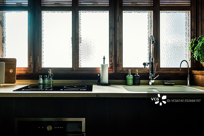 现代开放式厨房的温馨内饰，配有厨房用品和烹饪用具，阳光透过窗户照射进来图片素材