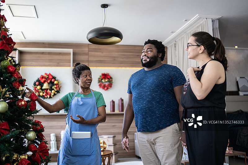 女销售员在装饰品店帮助顾客夫妇购买圣诞树图片素材