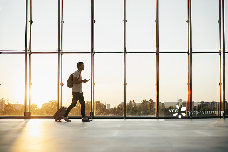 商务男士在机场使用手机并拉着行李箱图片素材