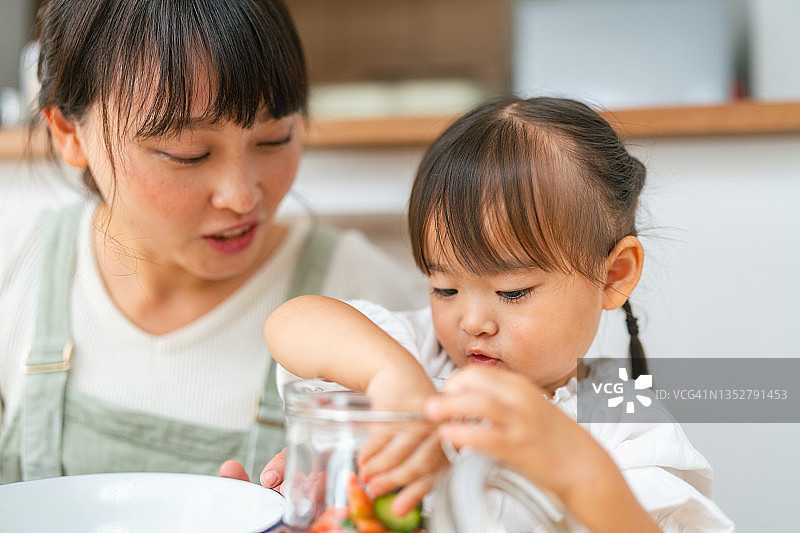 母亲和小女儿在家准备沙拉，帮助女儿准备蔬菜并鼓励她健康饮食图片素材