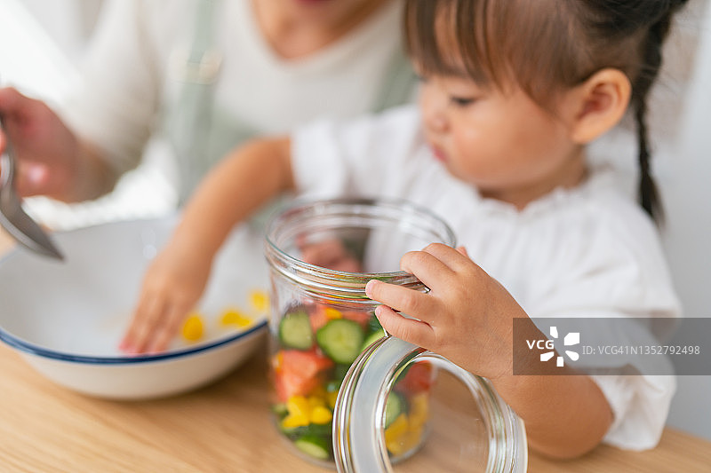 母亲和小女儿在家准备沙拉，帮助女儿准备蔬菜并鼓励她健康饮食图片素材