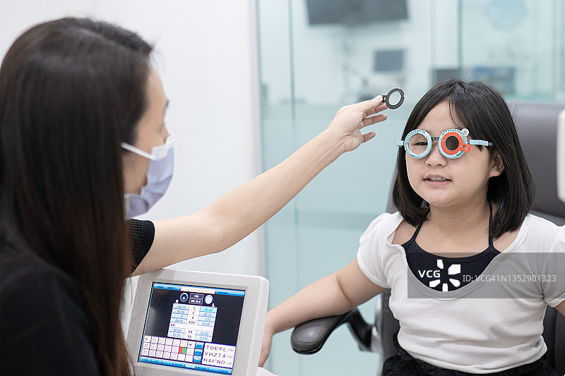 在眼科实验室里使用验光镜为儿童患者检查的中国女眼科医生图片素材