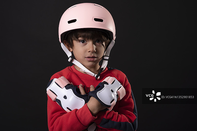 在黑色背景下手持滑板护具的男孩图片素材