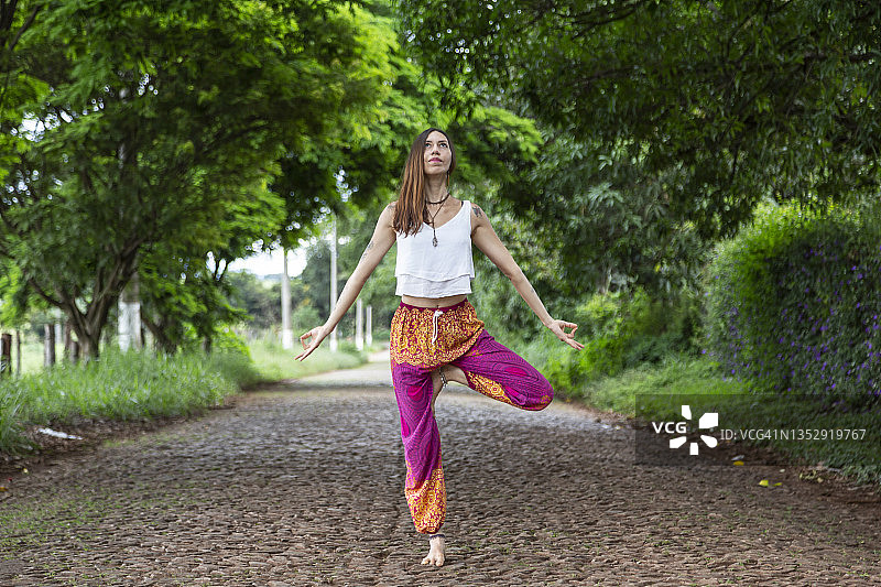 拉丁裔女子在乡间绿地道路上穿彩色裤子做瑜伽图片素材