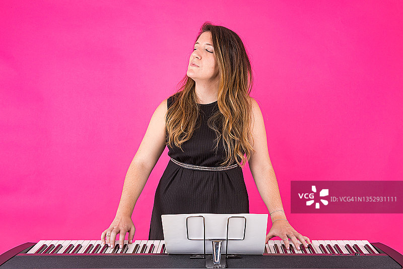 钢琴家女孩在粉色背景上闭着眼睛弹钢琴图片素材