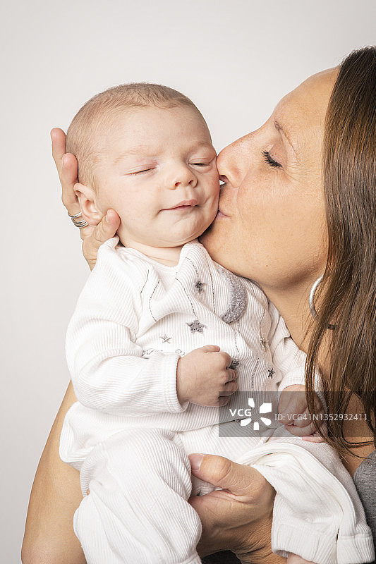 母亲亲吻熟睡的两个月大男婴图片素材