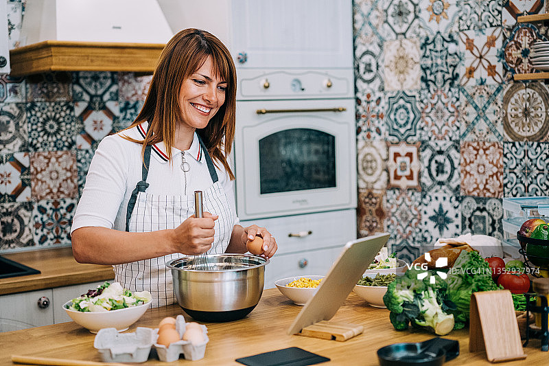 年轻女人在现代厨房里一边做午饭一边用平板电脑看菜谱图片素材