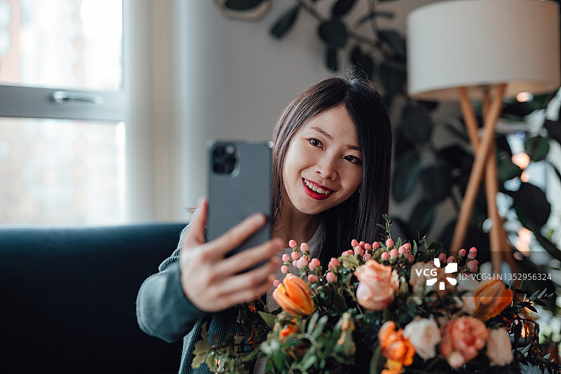 年轻女子手捧鲜花，用智能手机自拍图片素材