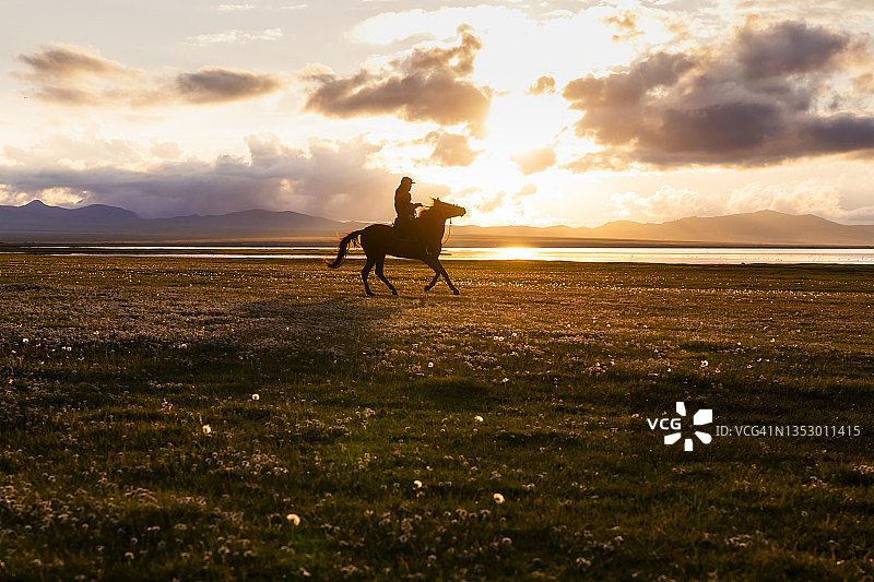 在吉尔吉斯斯坦宋科尔湖岸边日落时分的骑马者图片素材