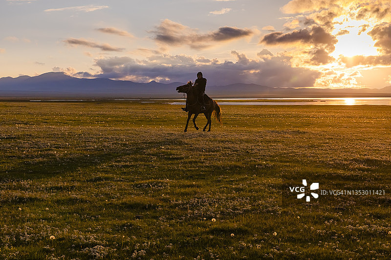在吉尔吉斯斯坦宋科尔湖岸边日落时分的骑马者图片素材