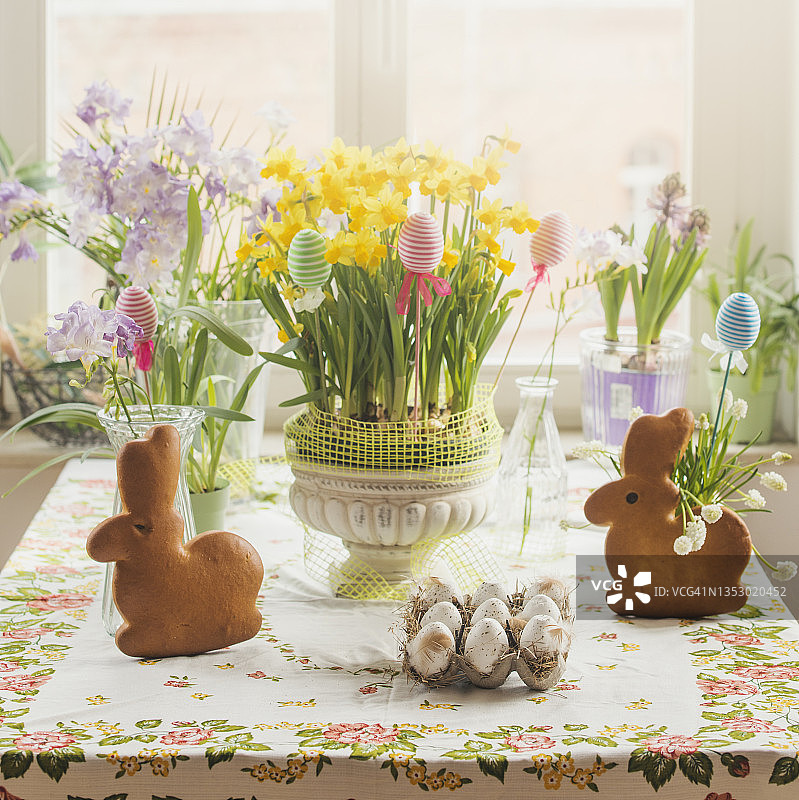 复活节餐桌，兔子造型糕点、复活节彩蛋、黄水仙、复活节装饰品和彩色春季鲜花，窗户背景。图片素材