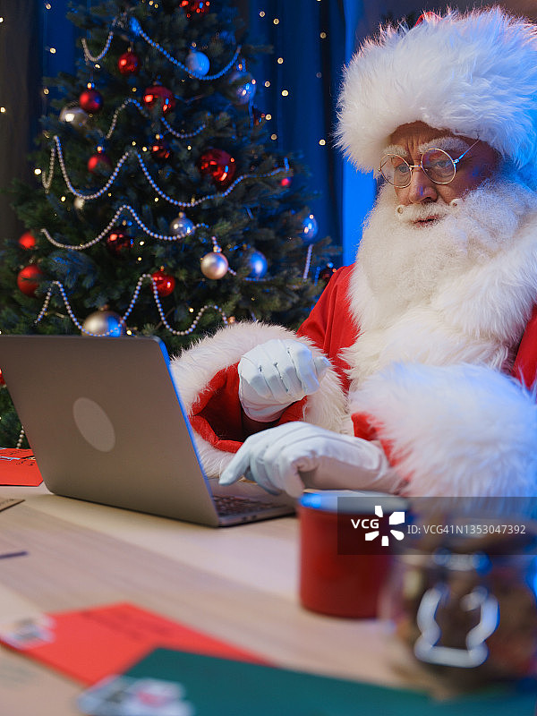 圣诞老人在圣诞树旁用笔记本电脑发短信图片素材