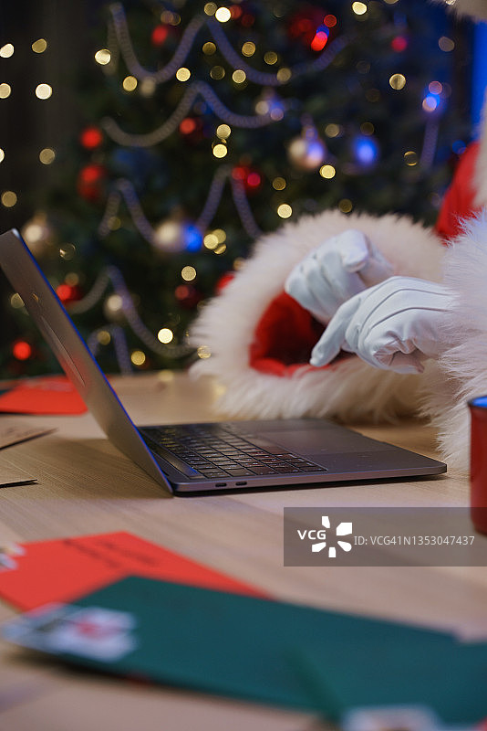 戴着白色手套的圣诞老人用笔记本电脑键盘打字的特写，背景是圣诞树图片素材