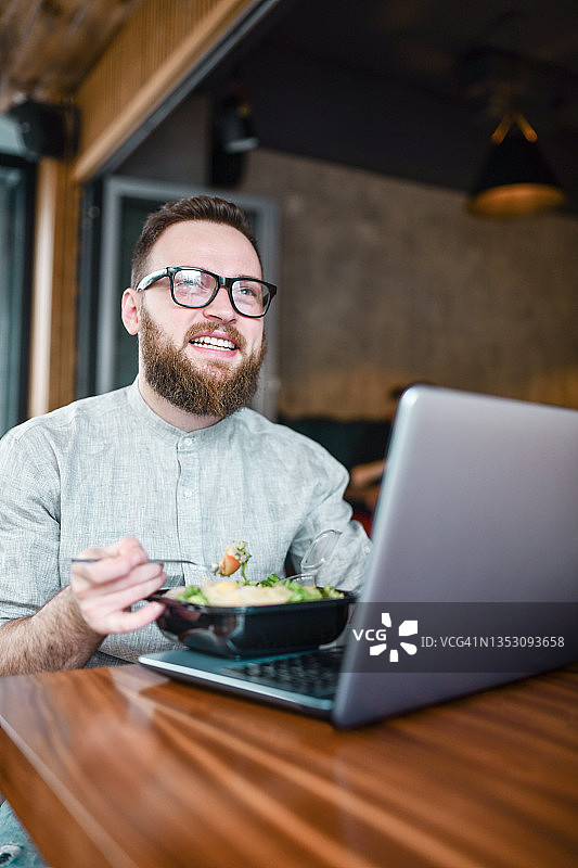 面带微笑、留着胡须的男子在餐厅吃鸡肉沙拉图片素材