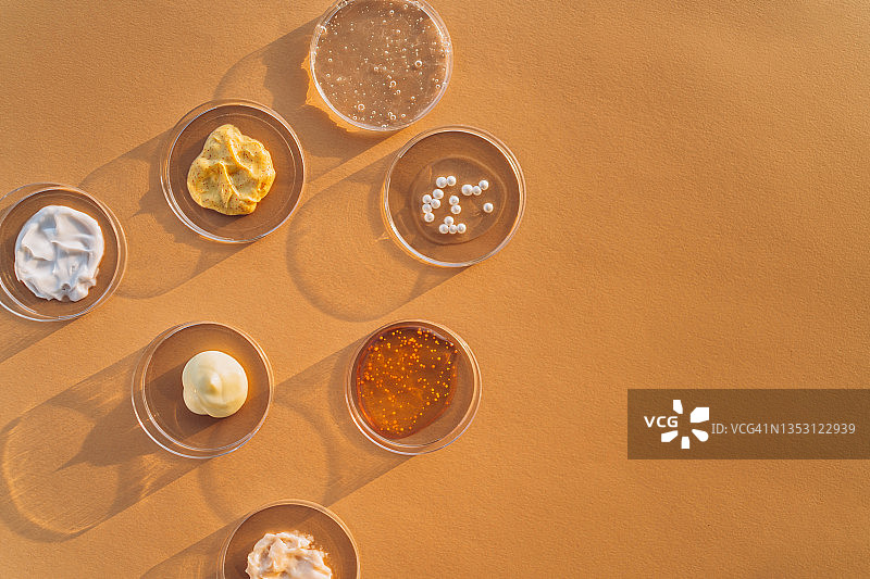 米色背景下的培养皿中盛放的彩色乳霜、磨砂膏、面部精华和凝胶，化妆品实验室研究概念，扁平风格摄影，含文案空间图片素材