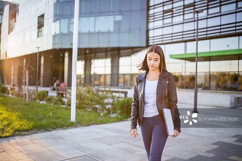 年轻女学生带着笔记本电脑在户外行走图片素材