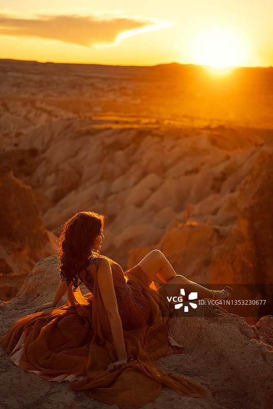 年轻女子坐在悬崖边看日落的背影图片素材