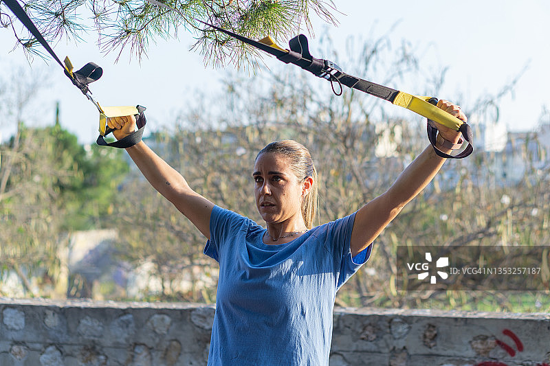 年轻拉丁女人在公园用两根弹力带锻炼肩膀图片素材