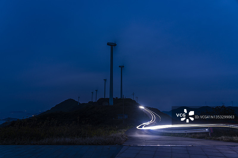 风力涡轮机、灯光和车辆在弯曲的山路上行驶的轨迹图片素材