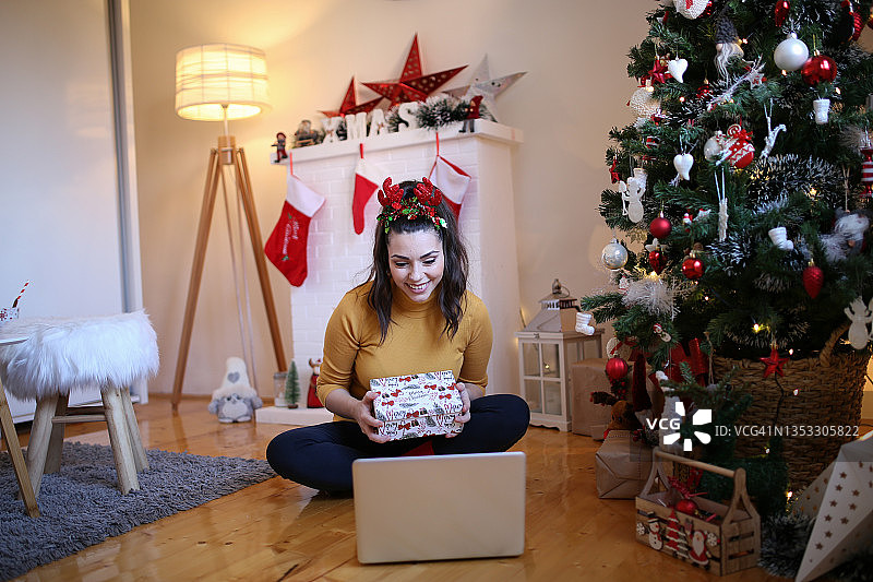 在家庆祝：快乐的女人在笔记本电脑上进行视频通话时打开圣诞礼物图片素材