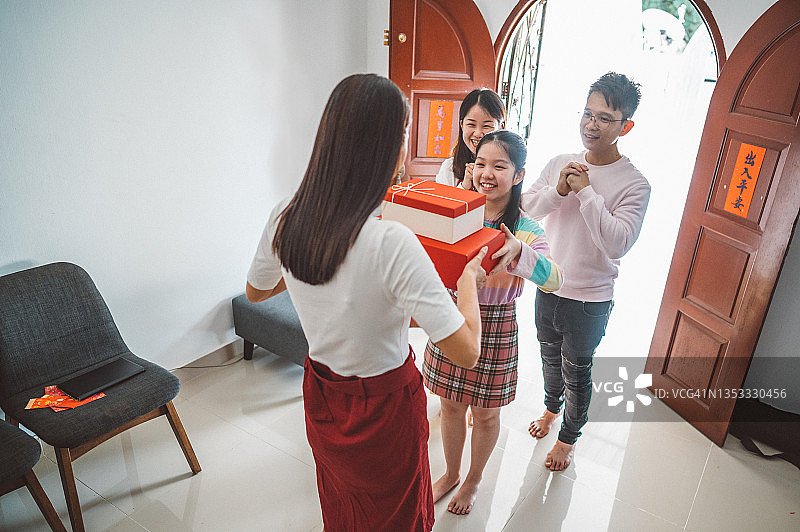 拜访亲戚家，在农历新年期间赠送礼物和食物的年轻漂亮亚洲少女与父母图片素材